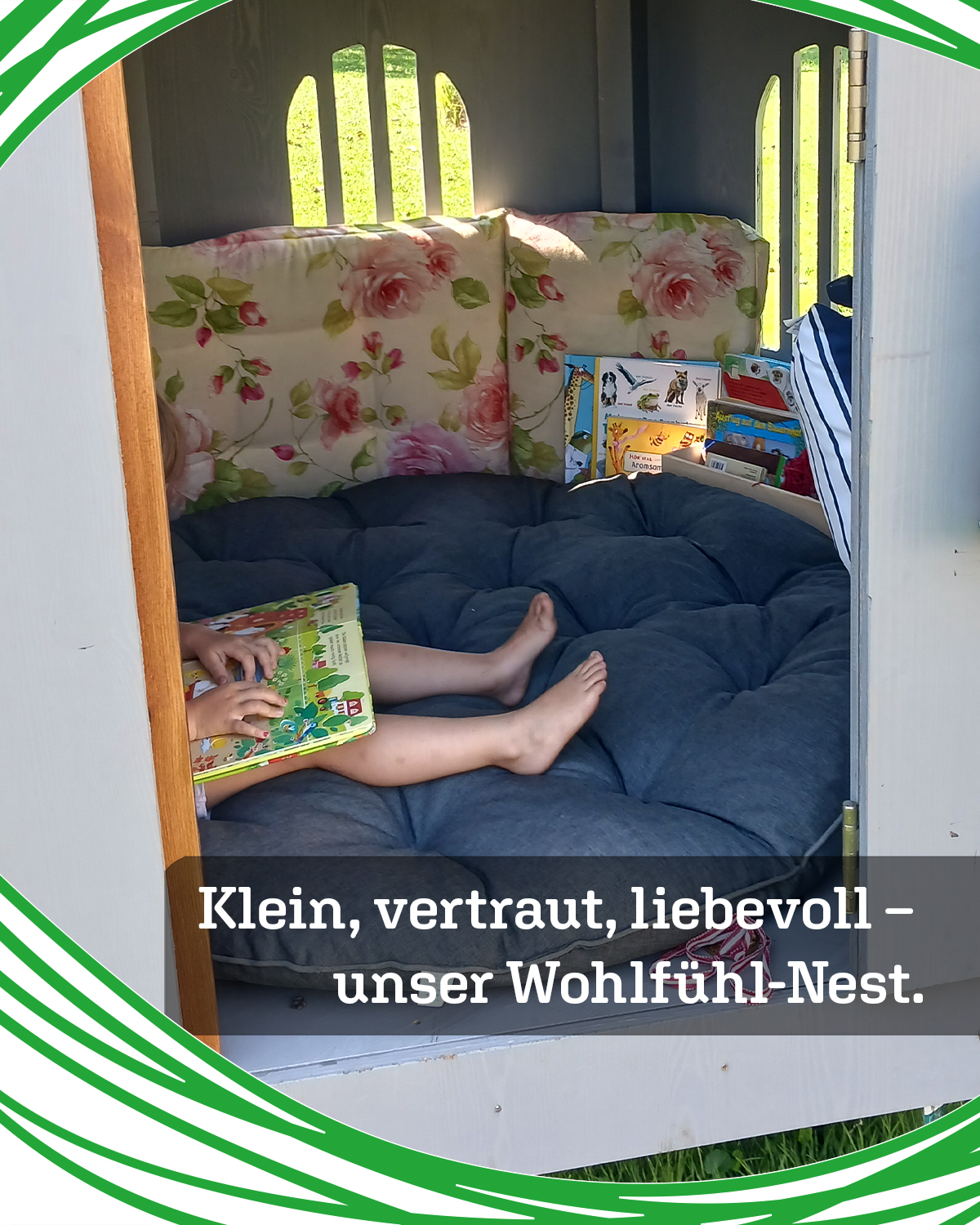 A child sits barefoot in a cozy blue cushioned nest inside a small wooden nook, reading a colorful picture book with shelves of children's books nearby and floral cushions behind.