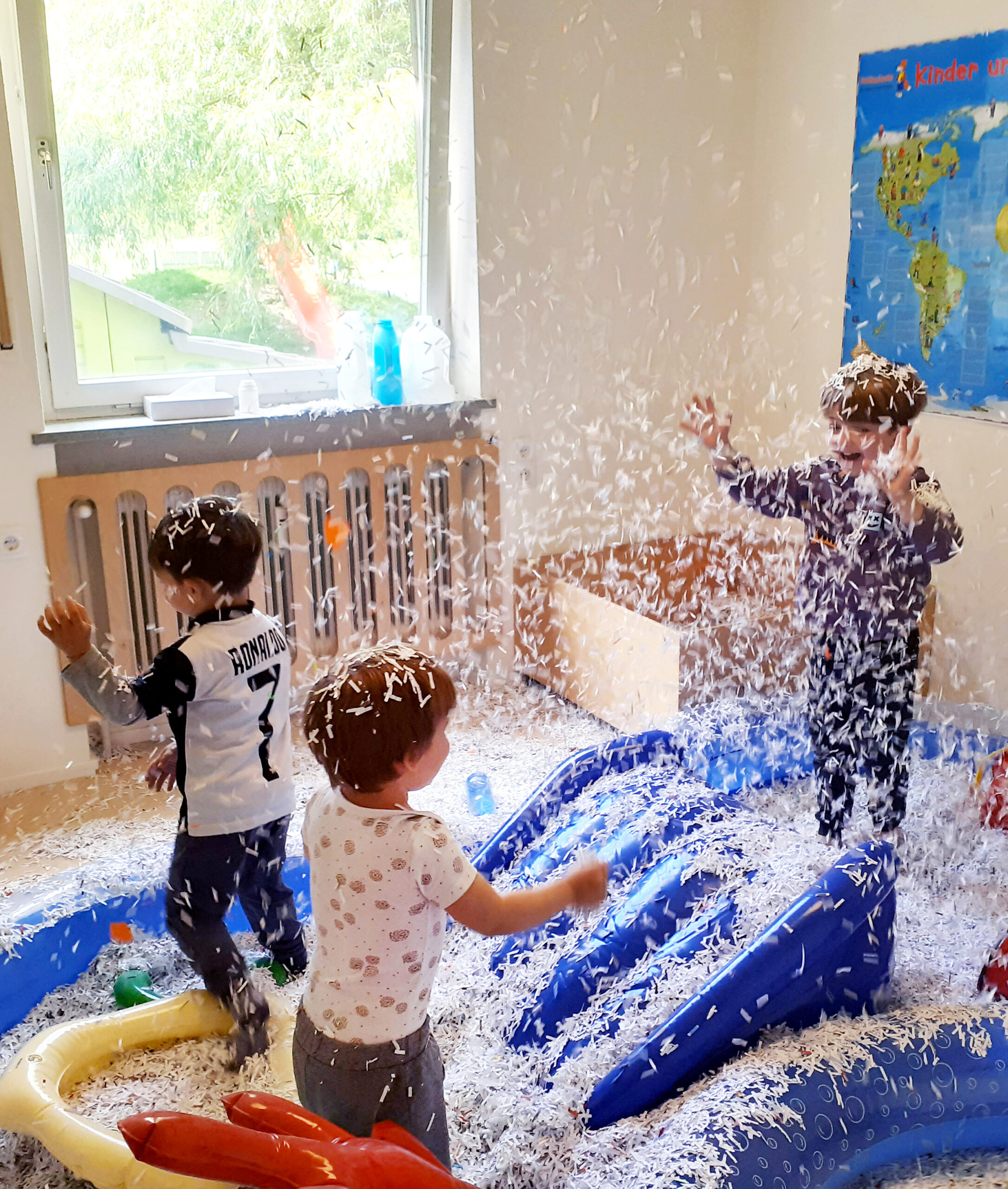 Aktion "PARKplatz": 3 Kinder im Zwergengarten Neuner spielen in einem blauen Schwimmbecken mit Rutsche mit Papierschnipseln. (c) KibeV