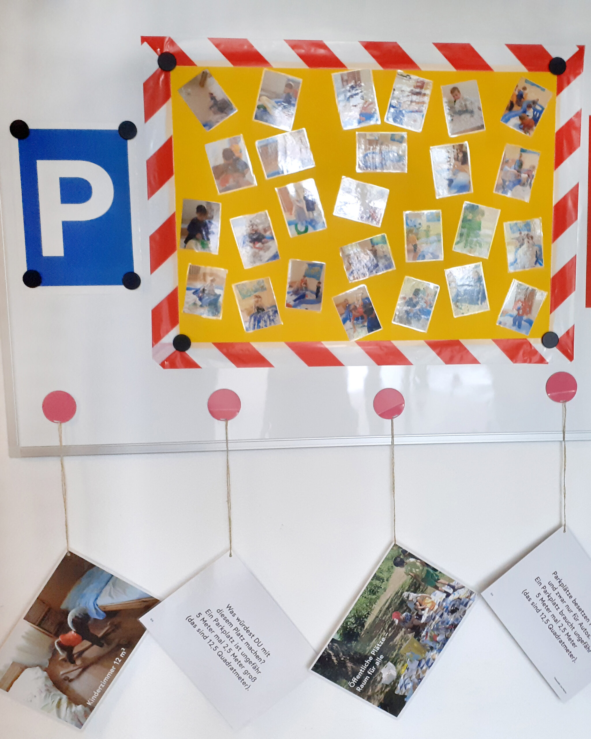 Aktion "PARKplatz": Weiße Magnettafel mit einer eingezeichneten Parkplatzfläche und einem blauen Parkplatzschild davor. Darauf sind verschiedene Fotos von Kindern. Darunter sind 4 Blätter mit Erklärungen für die Erziehungsberechtigte, die mit Schüren an runden roten Magneten befestigt wurden. (c) KibeV