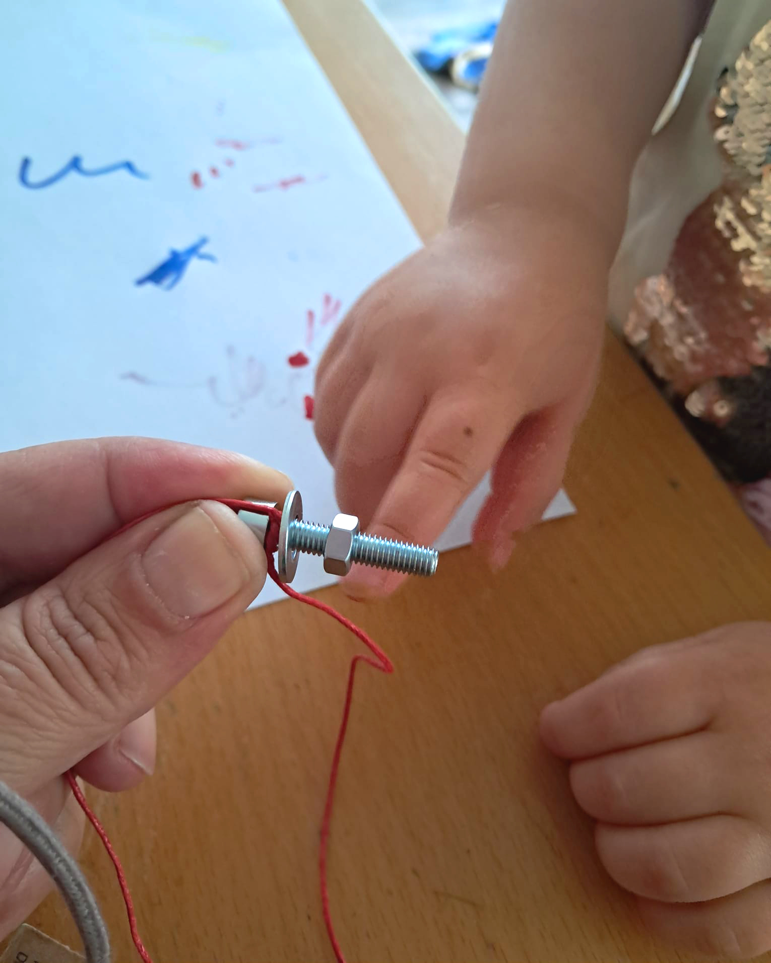Erwachsenenhand hält eine Schraube, auf die eine Kinderhand eine Mutter daraufschraubt. (c) KibeV