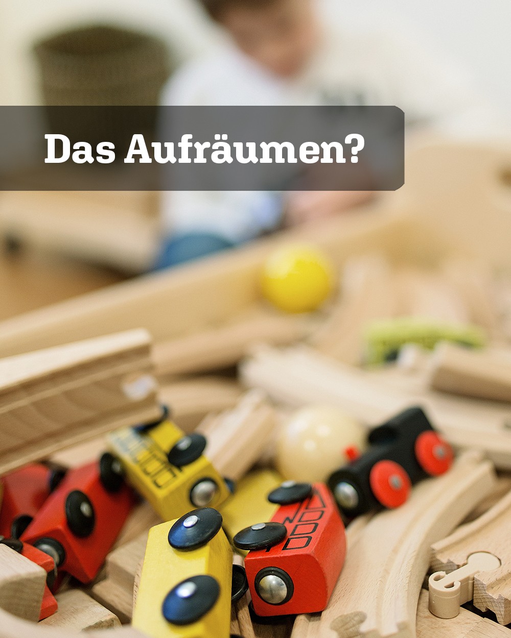 'Das Aufräumen?' steht über einem Bild mit Holz-Eisenbahnwaggons. Im Hintergrund sitzt verschwommen ein Kind. (c) KibeV
