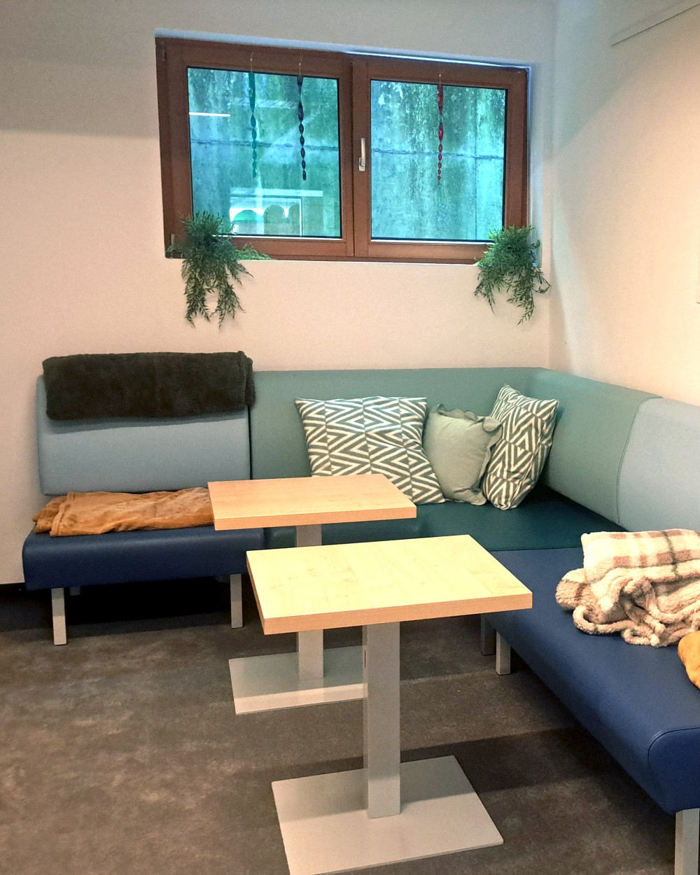 L-shaped blue sectional couch with patterned cushions and two small wooden tables in a cozy room at home or office.
