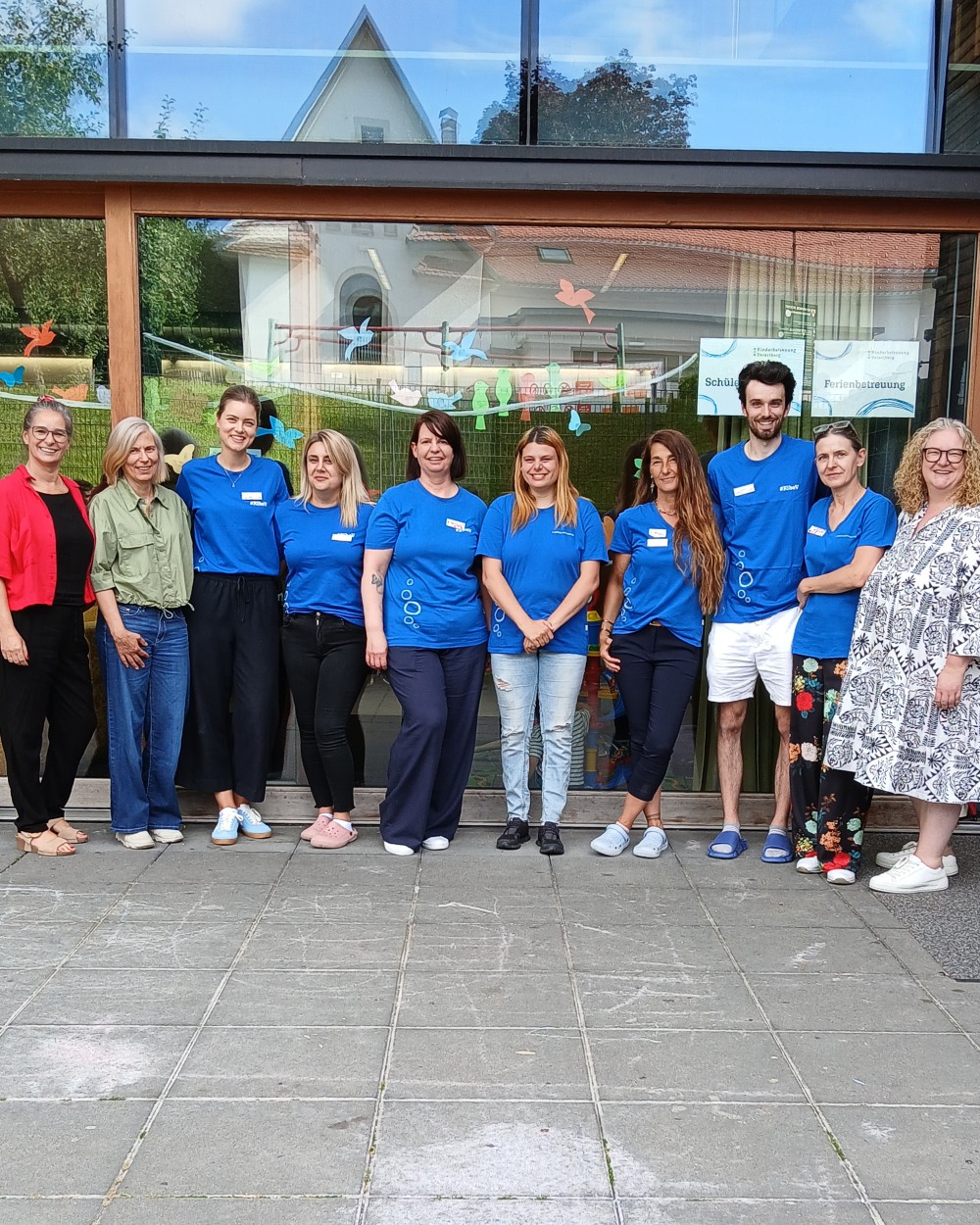 Group of people standing in a line outside a glass-front building, many wearing blue shirts and name badges, posing for a photo.