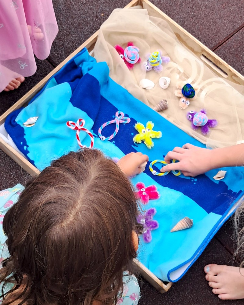 Kinder spielen mit einem Aktionstablett zum Thema "Fische". (c) KibeV