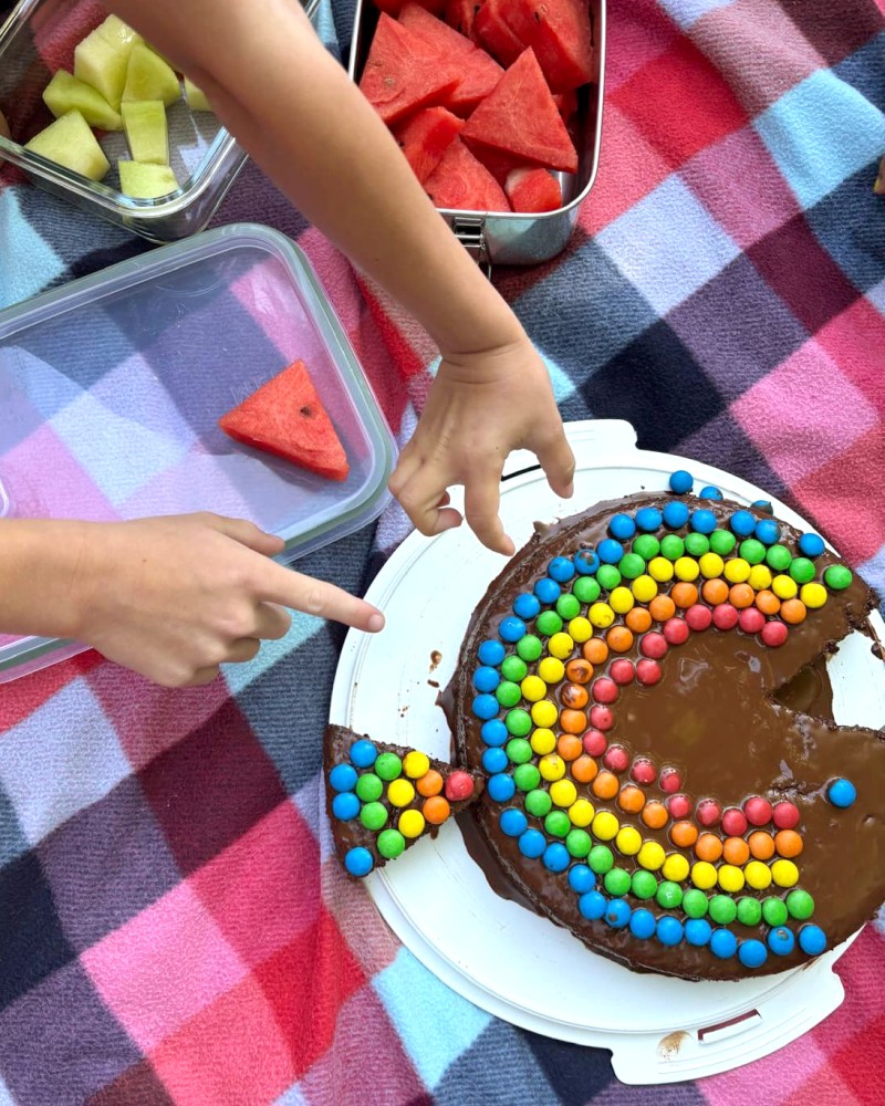 Kinderhände dekorieren einen Regenbogenfischkuchen. (c) KibeV