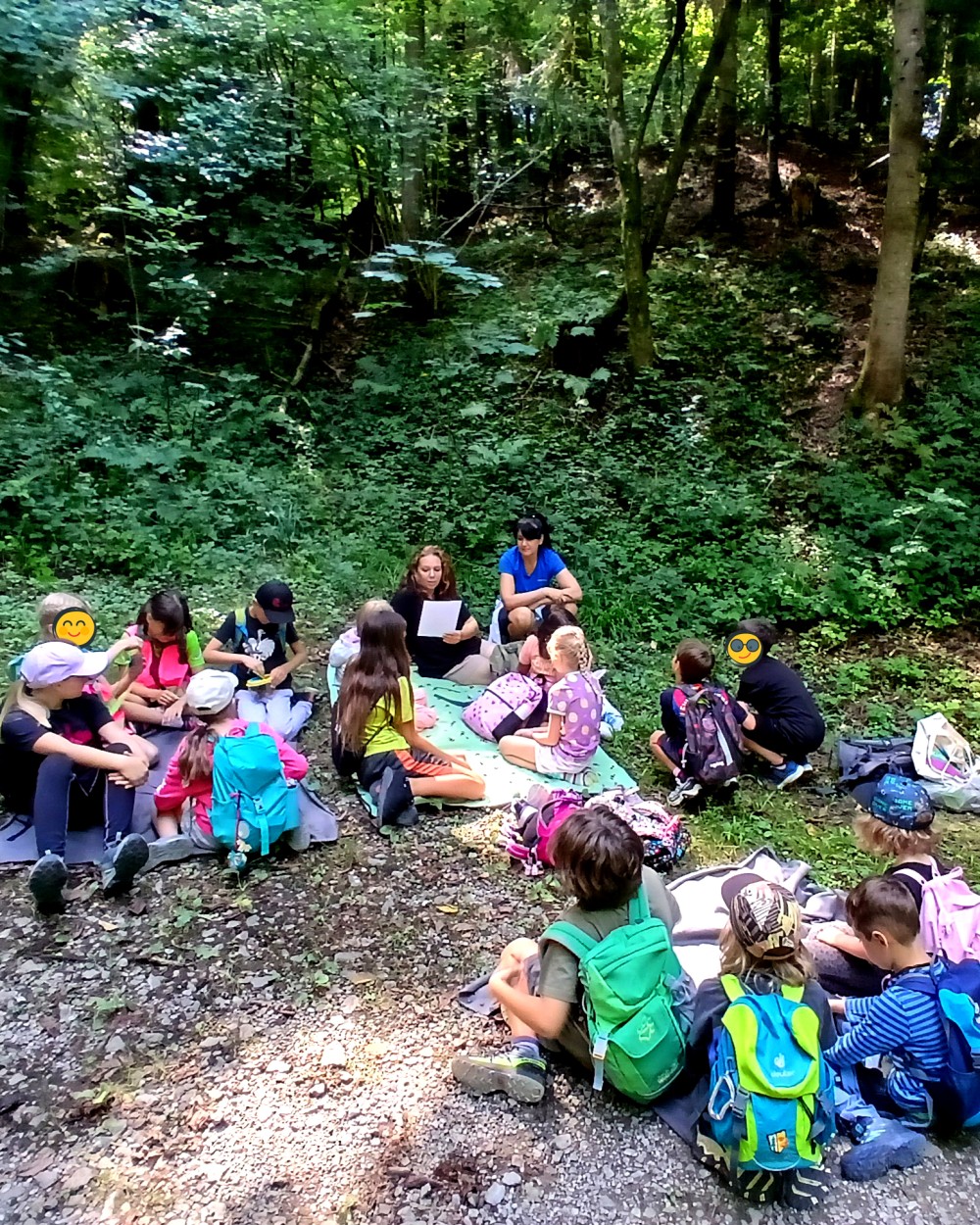 Kinder und Betreuerinnen der Ferienbetreuung Schwarzach sitzen auf einer Waldlichtung und bereiten sich auf den Waldtag vor. (c) KibeV