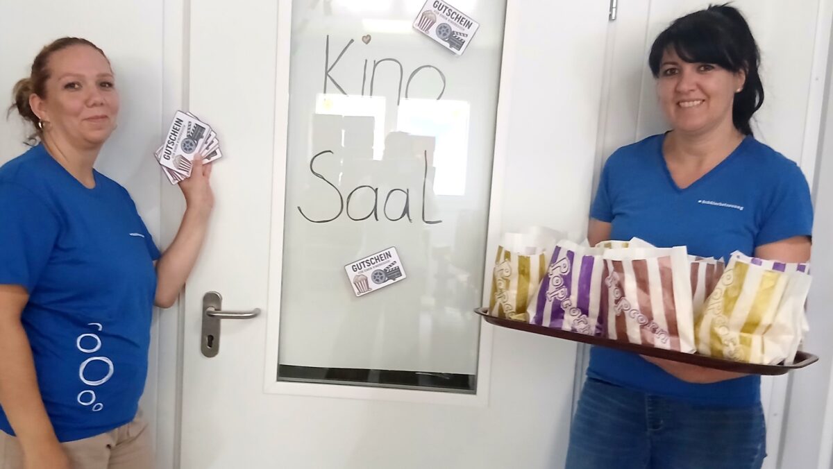 Zwei Betreuerinnen der Ferienbetreuung Schwarzach stehen mit Popcorn und Eintrittskarten vor dem "Kinosaal" in ihrer Einrichtung. (c) KibeV