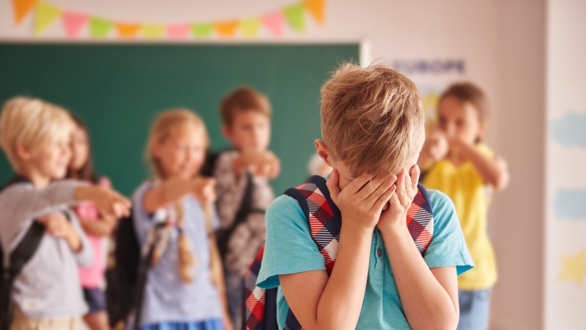 Im Vordergrund steht ein weinender Junge mit dem Gesicht in den Händen versteckt. Im Hintergrund ist eine Gruppe Kinder zu sehen, die auf den Jungen zeigt und lacht. (c) gpointstudios, magnific.com